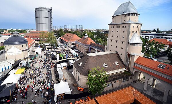 Luftaufnahme einer Menschenmenge mit verschiedenen Ständen auf dem Gaswerksgelände. Weiterverlinkung auf nächsten Schritte 2020 Newsartikel