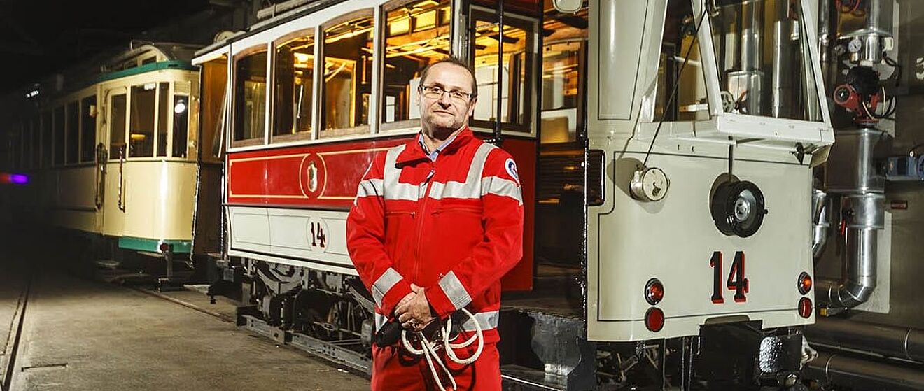Im Vordergrund steht ein Mann in Wasserwachtkleidung. Im Hintergrund befindet sich eine historische Straßenbahn. 