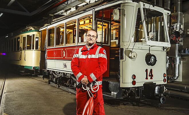 Im Vordergrund steht ein Mann in Wasserwachtkleidung. Im Hintergrund befindet sich eine historische Straßenbahn. 