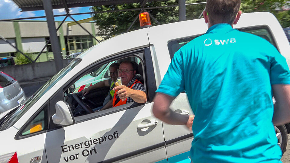 Swa Mitarbeiter sitzt in einem Auto und lacht in die Kamera.