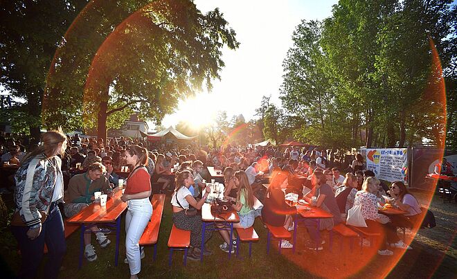 Fröhliche Menschen sitzen an Biertischgarnituren auf dem Historischen Gaswerk