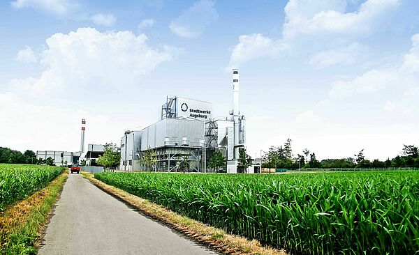 Grüner Feldweg mit Biomasse-Heizkraftwerk und einem roten Auto im Hintergrund