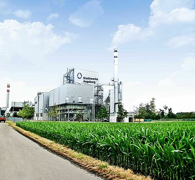 Grüner Feldweg mit Biomasse-Heizkraftwerk und einem roten Auto im Hintergrund