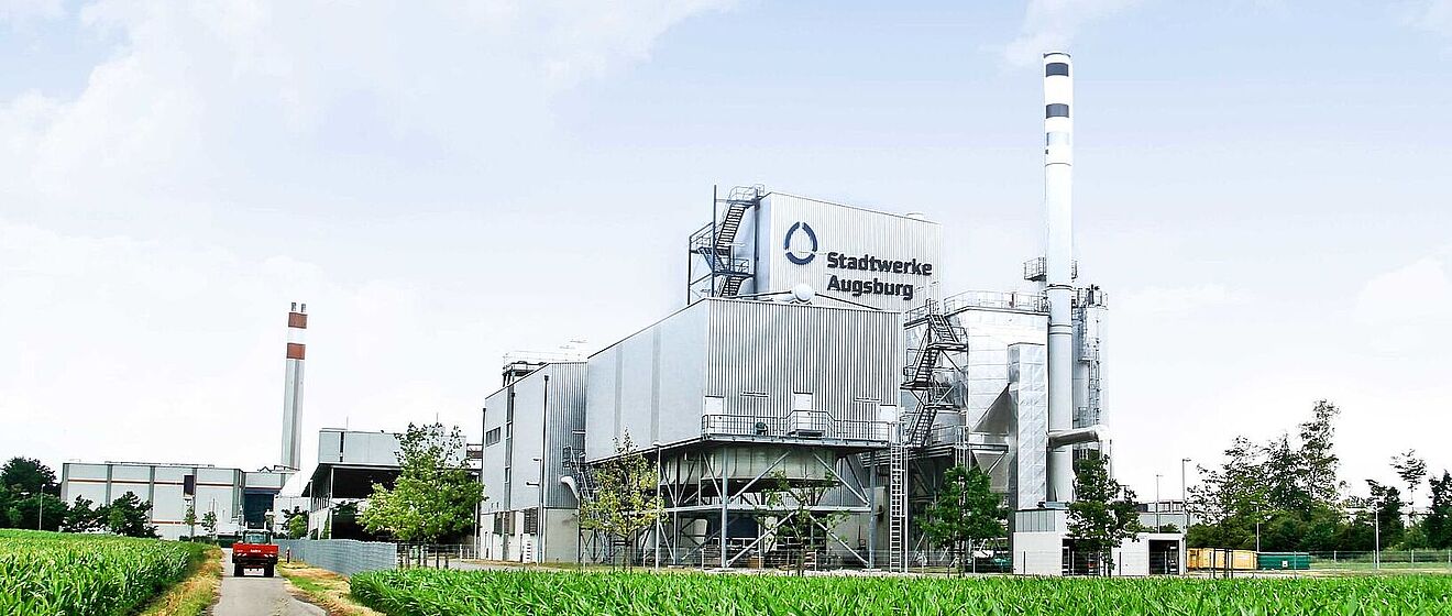 Grüner Feldweg mit Biomasse-Heizkraftwerk und einem roten Auto im Hintergrund
