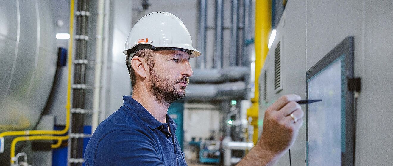 Mann mit Helm schreibt etwas auf einen Bildschirm an der Wand.