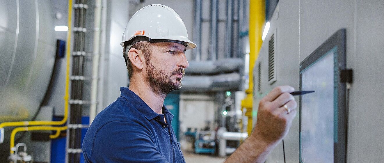 Mann mit Helm schreibt etwas auf einen Bildschirm an der Wand.