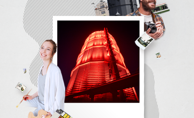 rot beleuchtetes Gaswerk in Bilderrahmen. Außerhalb des Rahmens sind zwei Personen mit Kamera und Pinsel in der Hand. Weiterverlinkung auf ARTram Newsartikel