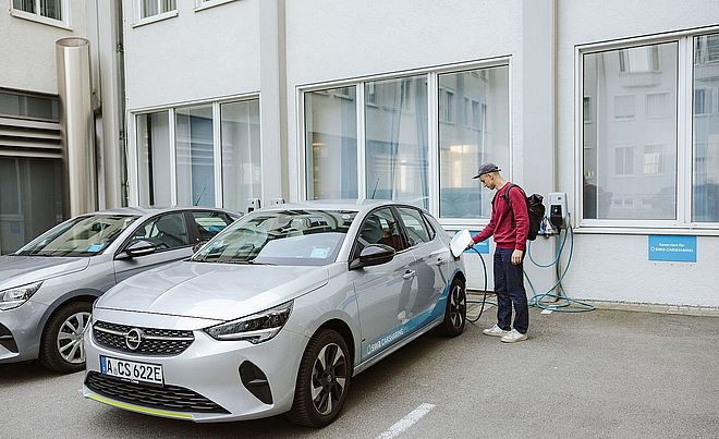 Ein Mann schließt ein swa Carsharing-Elektroauto an einer Wallbox an einer swa Carsharing-Station an.