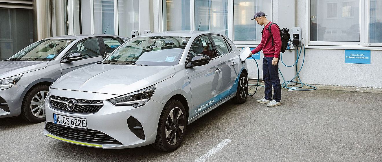 Ein Mann schließt ein swa Carsharing-Elektroauto an einer Wallbox an einer swa Carsharing-Station an.