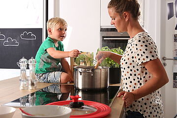 Kind schaut seiner Mutter beim Kochen zu. - Ein Klick auf das Bild führt zur vergrößerten Fotoansicht.