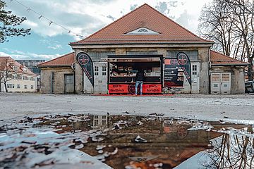 Person steht vor der Balkan Kitchen im Gaswerk während eine Person Essen vorbereitet.