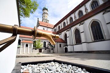 Trinkwasserbrunnen bei St. Ulrich in Augsburg. Im Hintergrund ist eine Kirche
