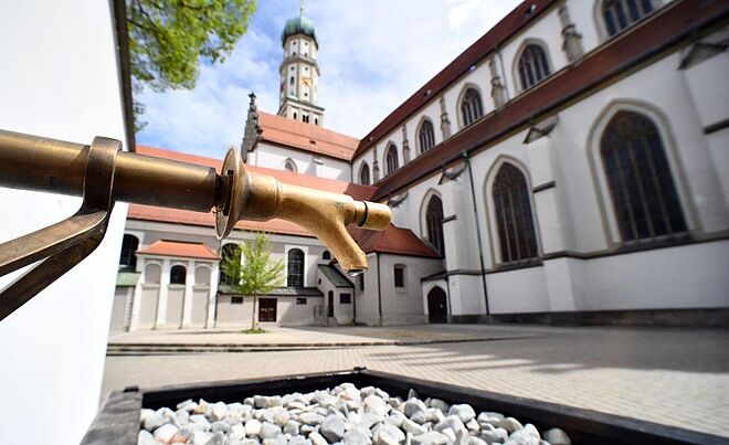 Trinkwasserbrunnen bei St. Ulrich in Augsburg. Im Hintergrund ist eine Kirche
