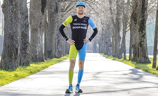 Triathlet Lukas Stahl auf einem Weg umgeben von Bäumen trägt einen Sportanzug und eine Kappe mit swa Logo