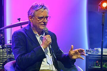 Mann mit Mikrofon sitzt vor Instrumenten. - Ein Klick auf das Bild führt zur vergrößerten Fotoansicht.