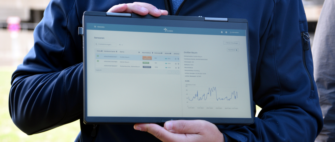 Person hält ein Tablet mit beiden Händen und präsentiert Daten auf dem Bildschirm.