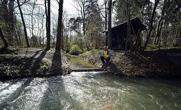 Mann sitzt neben Fluss im Wald