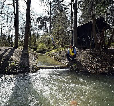 Mann sitzt neben Fluss im Wald