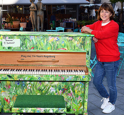 Bemaltes Klavier, in Grün Tönen. Frau lehnt sich an das Klavier an.
