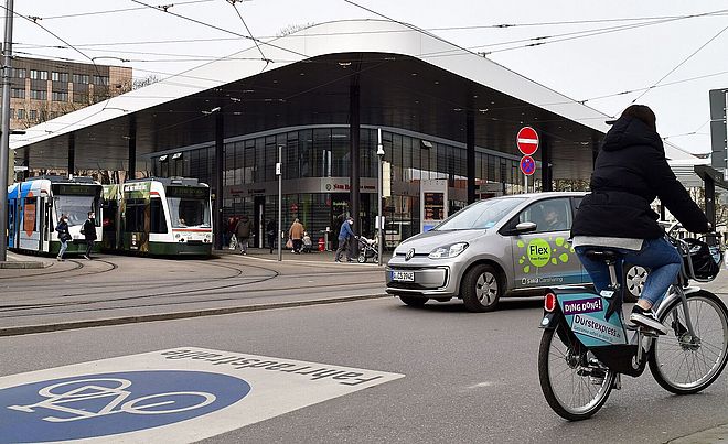 Foto vom Kö mit Bussen, einem Leihrad, einem swa Carsharing Auto und Trams.