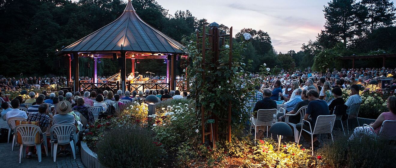 Lagrene / Farao / Gomez / White - 23. Int. Augsburger Jazzsommer Mann spielt Musik in einem Pavillon. Um ihn herum sitzt ein großes Publikum.
