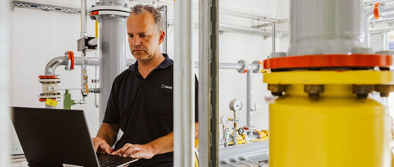 Mann tippt am Laptop und ist umgeben von Maschinentechnik