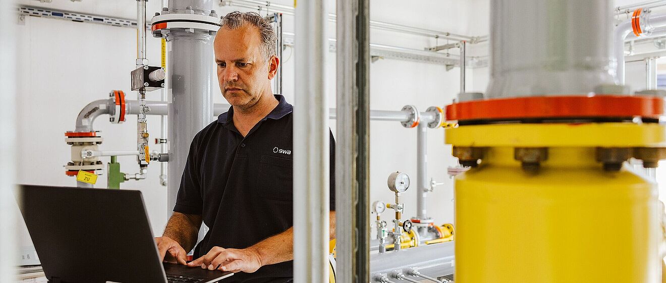 Mann tippt am Laptop und ist umgeben von Maschinentechnik