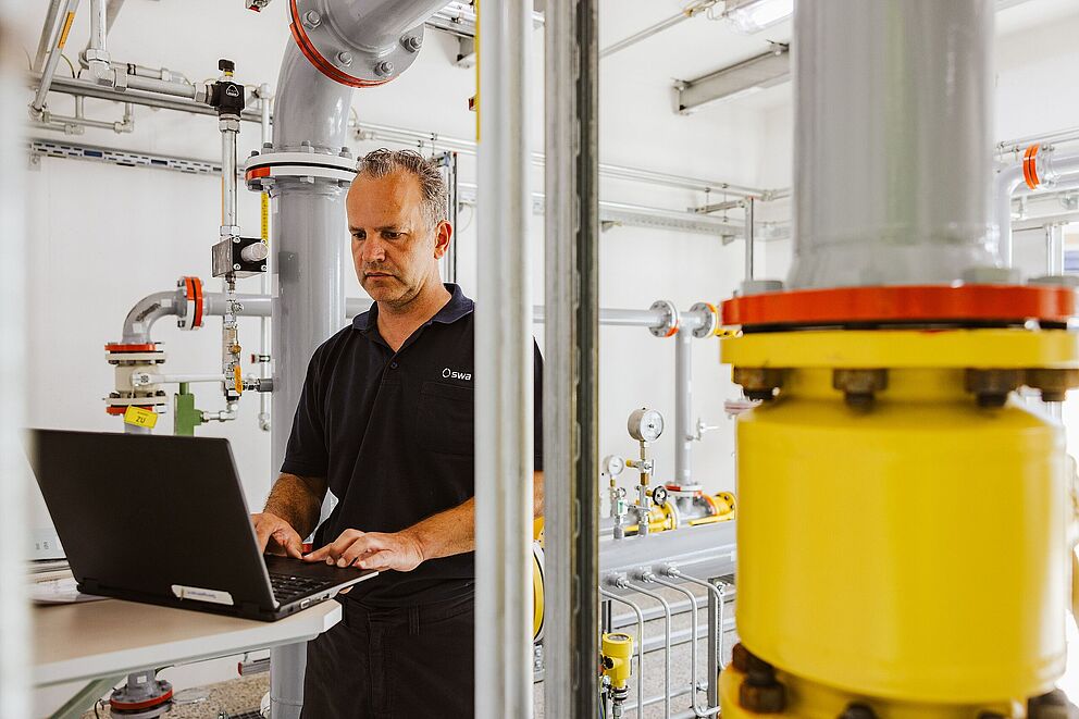 Mann tippt am Laptop und ist umgeben von Maschinentechnik
