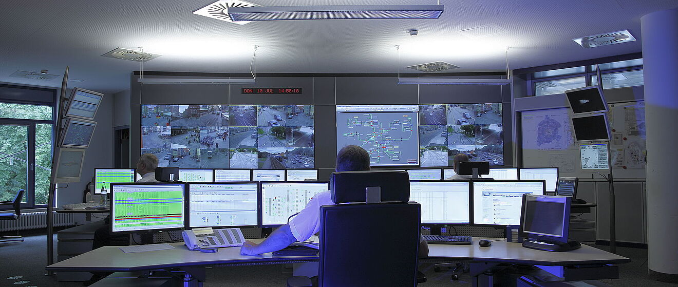 Leitwarte Ein Leitwarte von Hinten mit sehr vielen Bildschirmen vor ihm. Auf den Displays sind LIVE-Überwachungsaufnahmen von Straßenbahnen und Daten zu den Linien zu sehen zusammen mit vielen anderen Anzeigen.