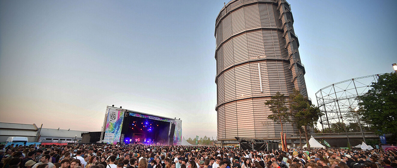 Menschenmenge auf dem Gaswerk beim Modular Festival. Im Hintergrund ist eine Bühne und der große Gasbehälter. Weiterverlinkung auf Modular 2023 Newsartikel