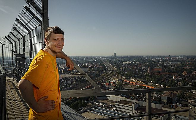 Mann steht auf Hausdach und lächelt in die Kamera