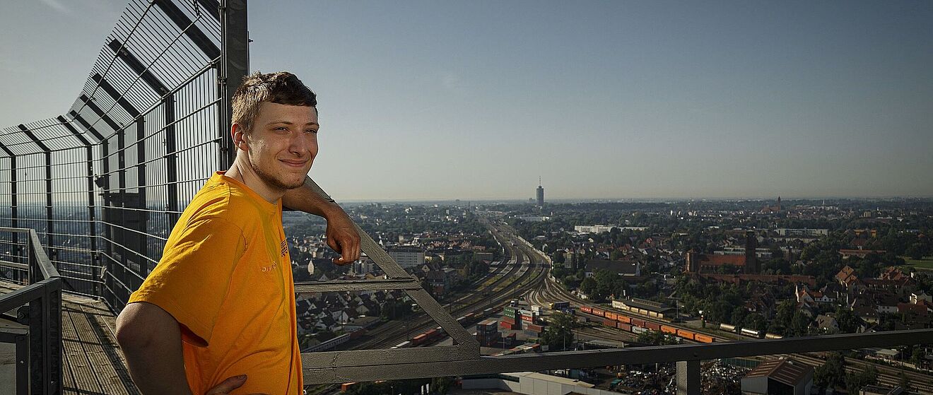 Mann steht auf Hausdach und lächelt in die Kamera