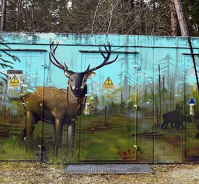 Bemaltes Häuschen im Wald. Gemalt ist ein Hirsch in der Landschaft.