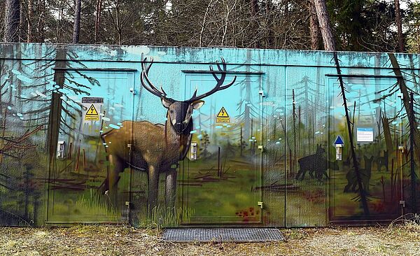 Bemaltes Häuschen im Wald. Gemalt ist ein Hirsch in der Landschaft.