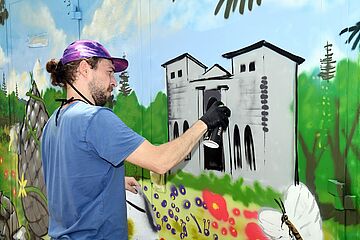 Eine Person malt mit Sprühdose ein Wandbild. - Ein Klick auf das Bild führt zur vergrößerten Fotoansicht.