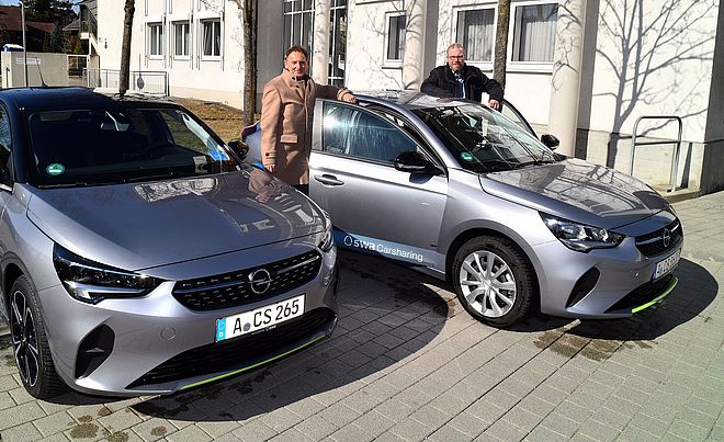 Zwei Männer stehen neben zwei Carsharing-Auto