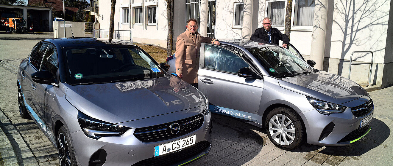 Zwei Männer stehen neben zwei Carsharing-Auto