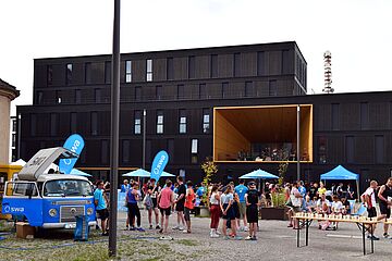 Menschen beim swa Spendenlauf. Links ist der swa Bulli, rechts ein Tisch mit Bechern und im Hintergrund eine Bühne