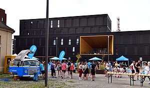 Menschen beim swa Spendenlauf. Links ist der swa Bulli, rechts ein Tisch mit Bechern und im Hintergrund eine Bühne