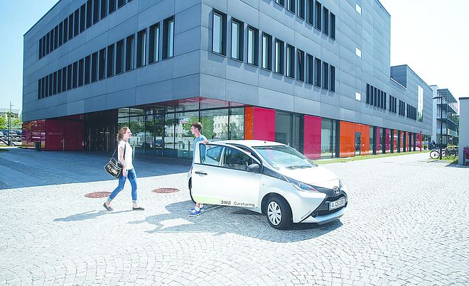 Ein Mann und Eine Frau stehen neben einem swa Carsharing-Auto vor einem Gebäude.