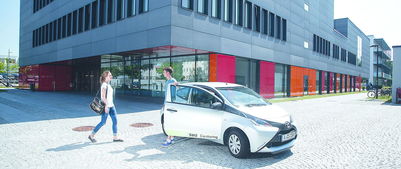 Ein Mann und Eine Frau stehen neben einem swa Carsharing-Auto vor einem Gebäude.