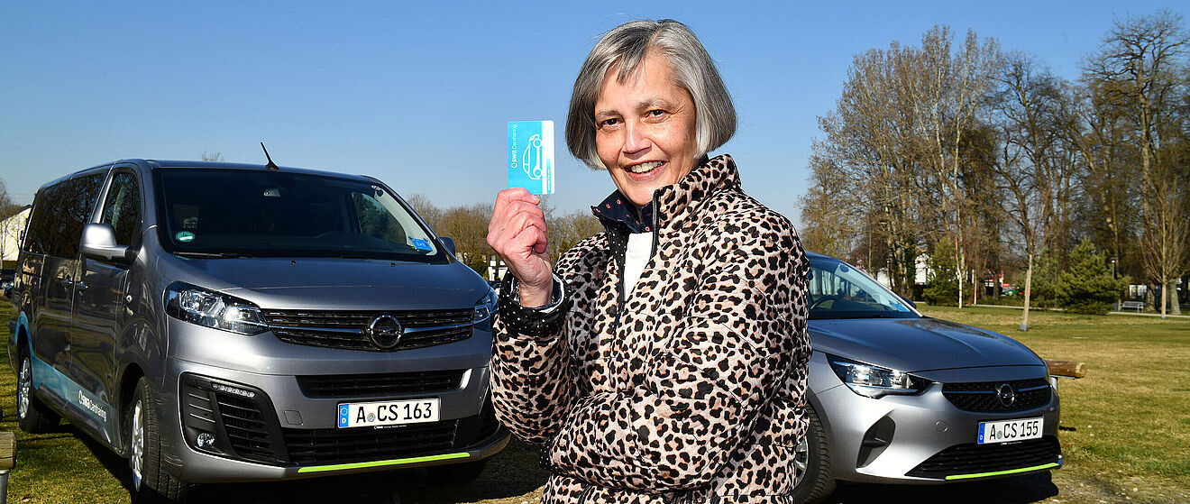 Frau mit Carsharingkarte steht vor Carsharing Autos