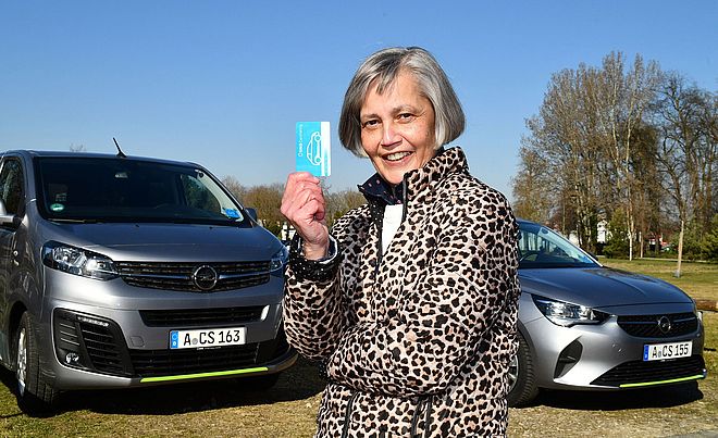 Frau mit Carsharingkarte steht vor Carsharing Autos