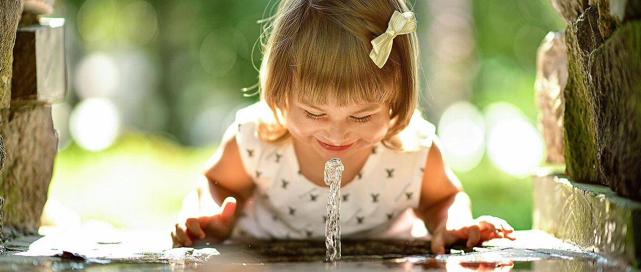 Kind schaut erstaunt Trinkwasser aus einem Trinkwasserbrunnen an
