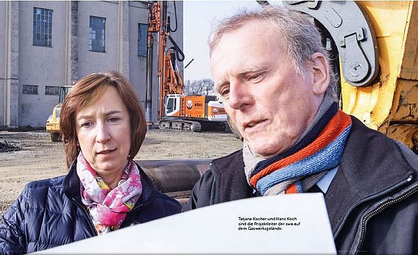 Ein Mann und eine Frau stehen nebeneinander. Im Hintergrund befindet sich eine Baustelle.