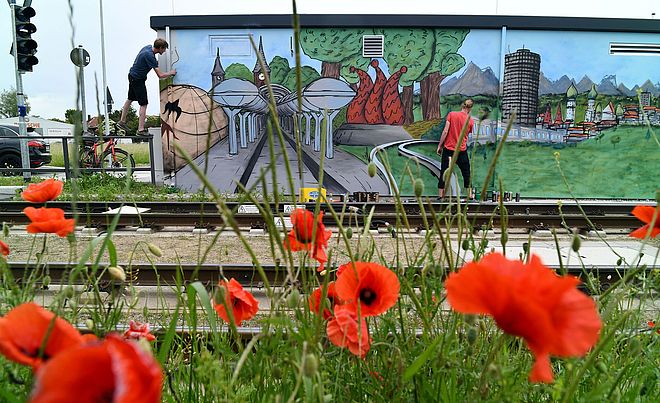 Von zwei jungen Männern wird ein Technikgebäude mit Graffiti verziert.