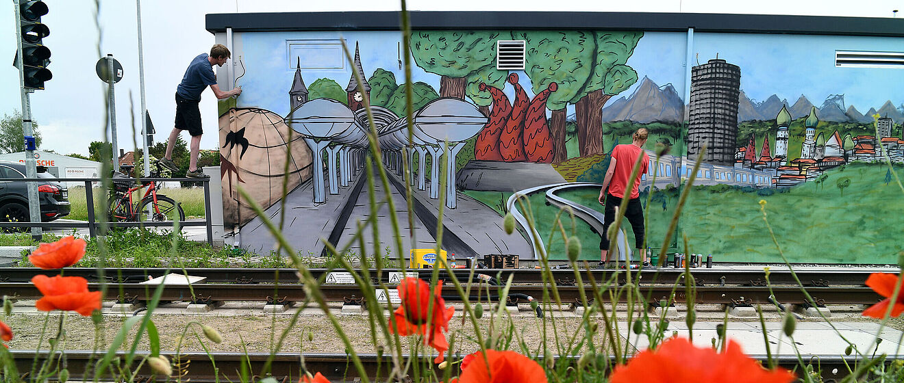 Von zwei jungen Männern wird ein Technikgebäude mit Graffiti verziert.